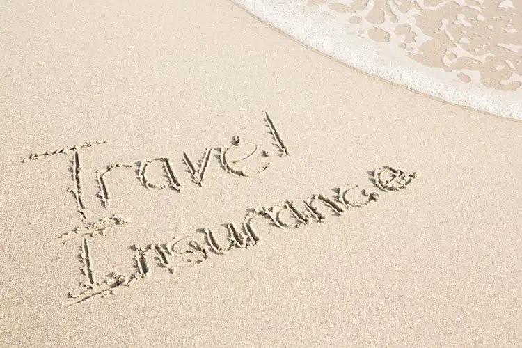 Travel insurance written on the beach sand