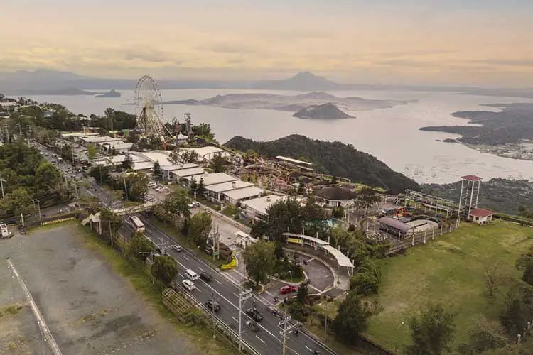 amusement park with a large ferris wheel and other rides, with views of Taal Volcano.